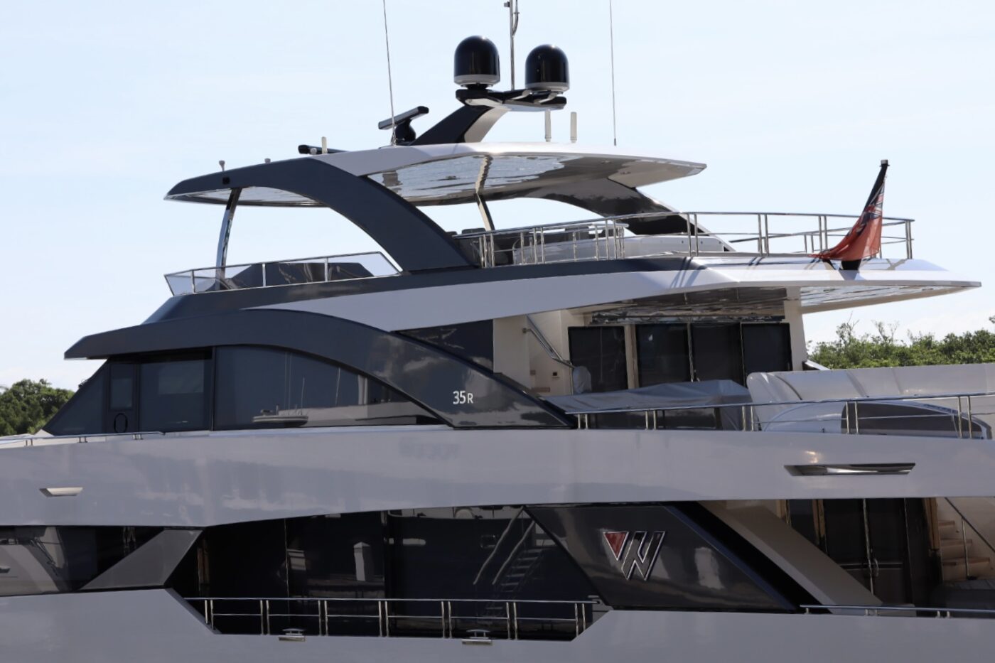 A sleek luxury yacht with a modern design, featuring multiple decks, large windows, and high-tech antennas, docked in a marina.