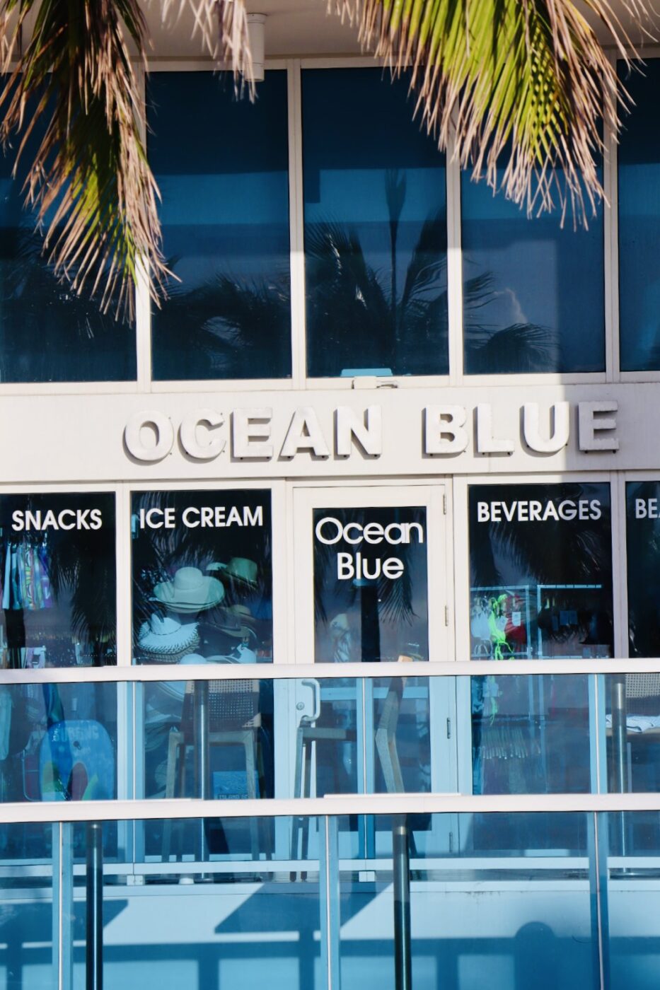 Ocean Blue storefront featuring large windows displaying snacks, ice cream, and beverages, set against a bright coastal backdrop.