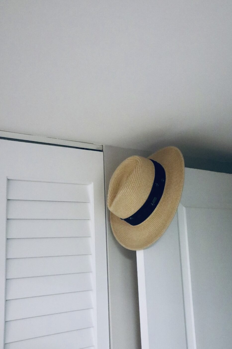 A straw hat with a black band hangs on the edge of a white closet door, suggesting a relaxed, summery vibe.