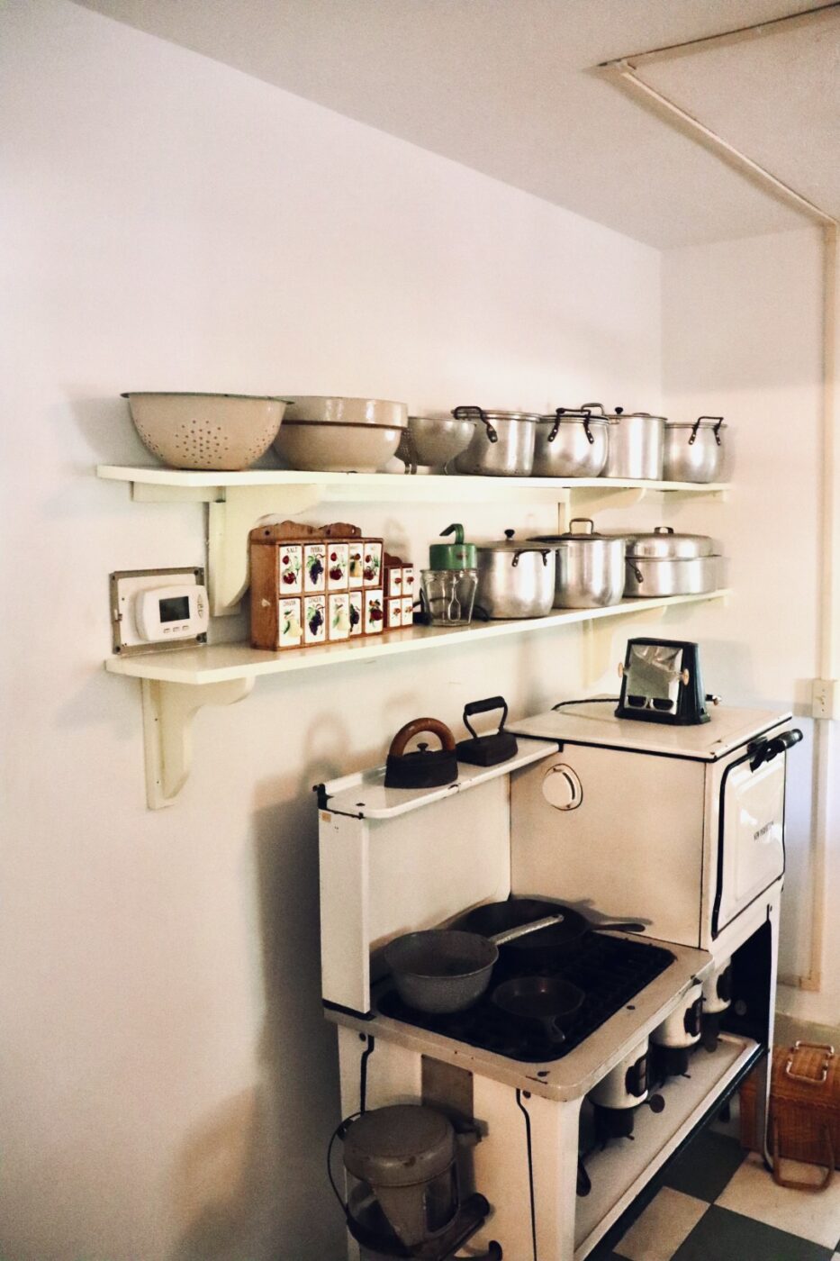 Vintage kitchen scene featuring a white stove with pots and pans, metal bowls on a shelf, and a colorful spice box, evoking a rustic culinary atmosphere.