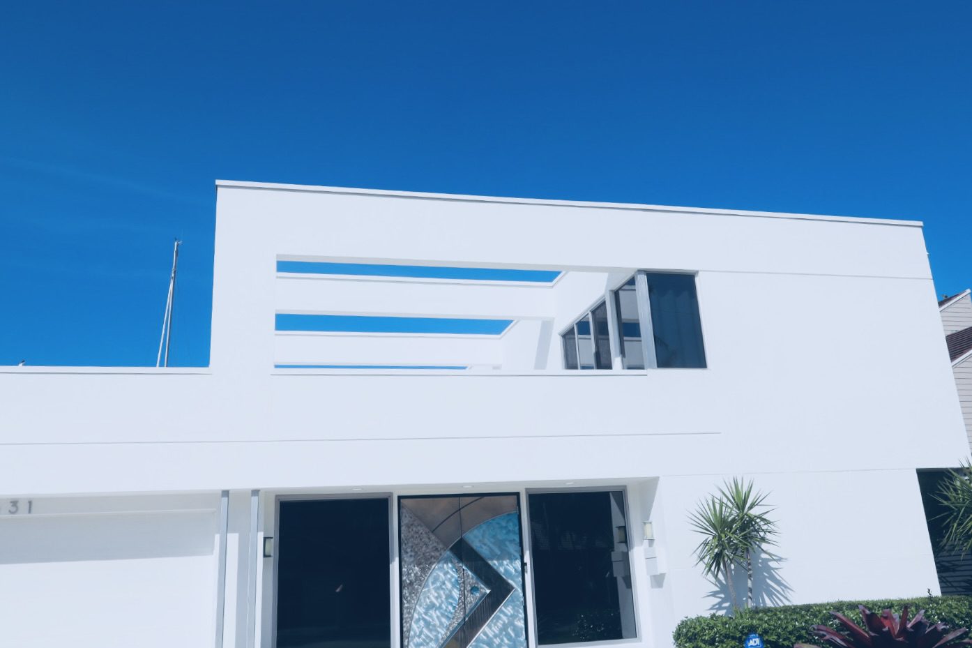 Modern white house with large windows and artistic door design, set against a clear blue sky, highlighting contemporary architecture.