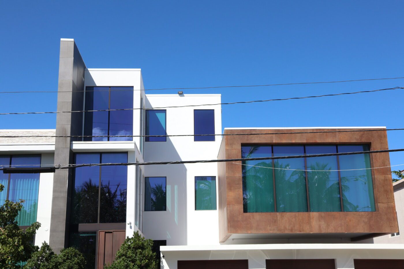 Modern two-story house featuring a blend of white and brown exteriors, large glass windows, and clear blue skies, showcasing contemporary architecture.