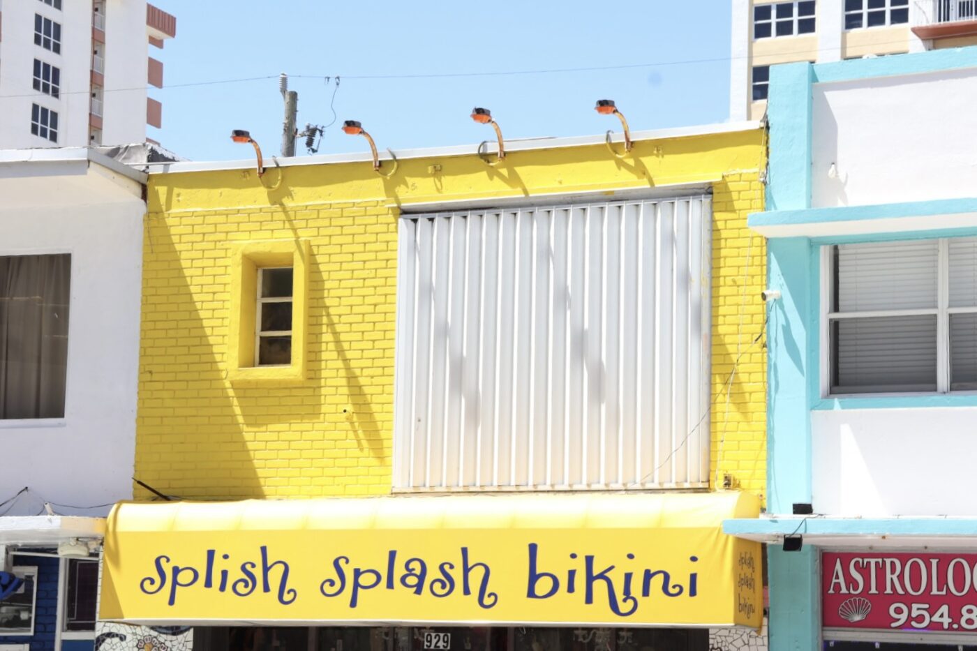 Bright yellow storefront with "splish splash bikini" signage, flanked by a white building and blue accents, captures a vibrant retail scene.