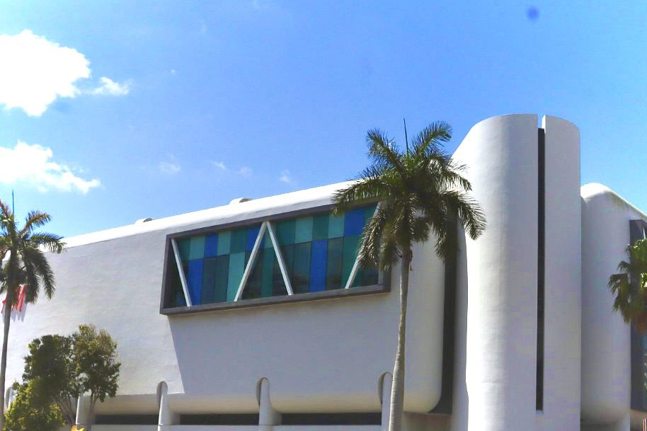 Modern architectural building featuring large windows and palm trees against a clear blue sky, reflecting contemporary design and vibrant surroundings.