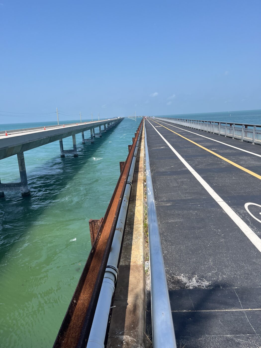 Dual coastal bridges extend into turquoise waters under a clear blue sky. One bridge is for vehicles, while the other is pedestrian-focused, showcasing connectivity.