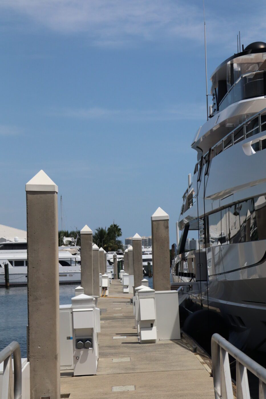 Luxury yacht docked alongside a well-maintained marina, with concrete pilings and service boxes lining the walkway under a clear blue sky.