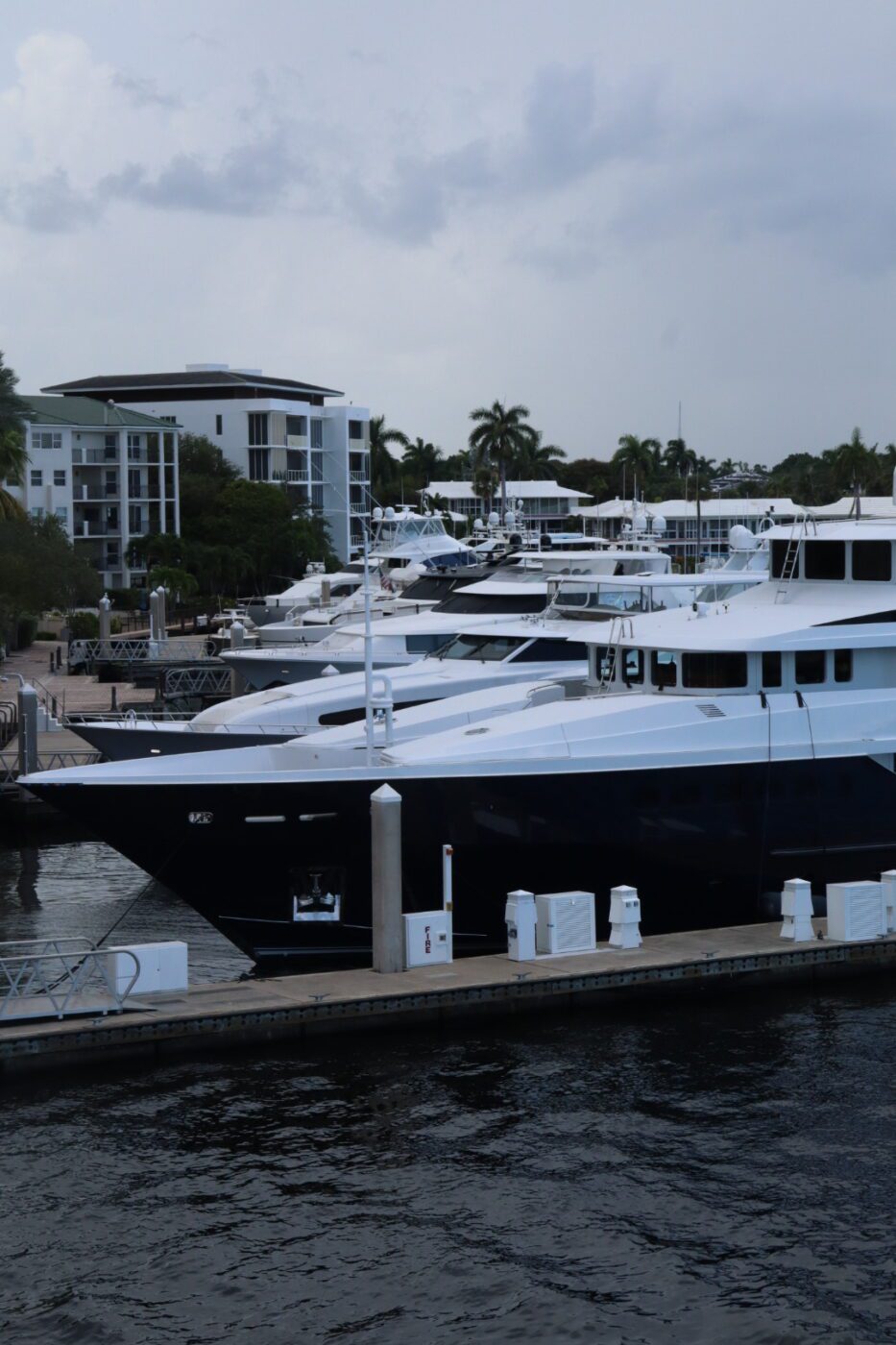 Luxury yachts docked along a marina, with modern waterfront buildings and palm trees in the background, highlighting a serene boating atmosphere.