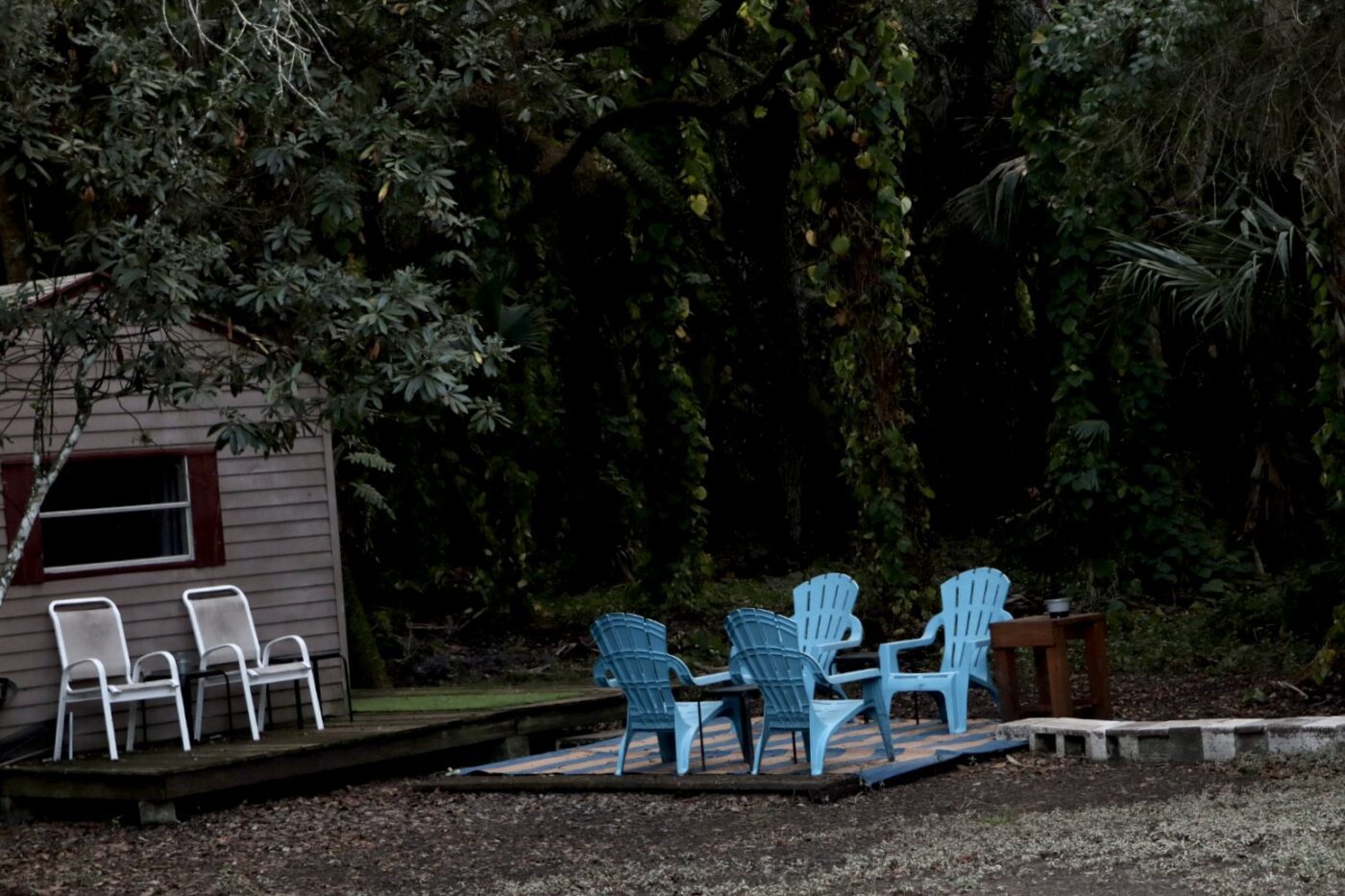 Cozy outdoor seating area with blue chairs and a small table, set against a lush, green backdrop. Perfect for gatherings or relaxation in nature.