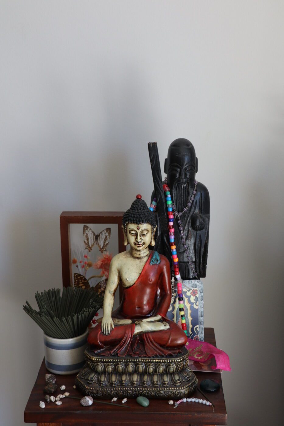 Buddha statue in a serene display, accompanied by a wooden figure, incense, and decorative items, reflecting spiritual themes and tranquility.